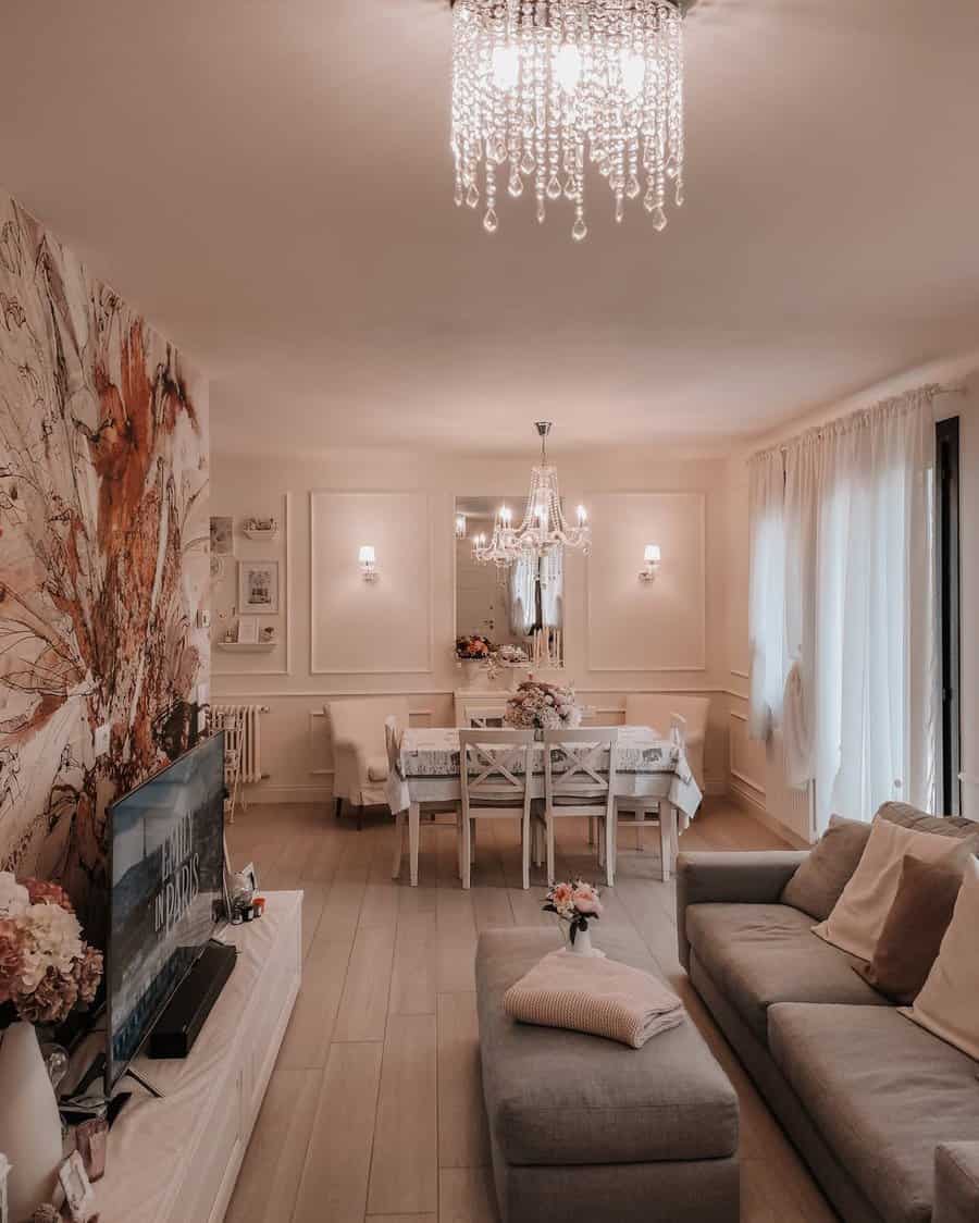 Elegant living and dining space with a soft neutral palette, crystal chandeliers, floral accents, and sheer curtains for a bright, airy feel