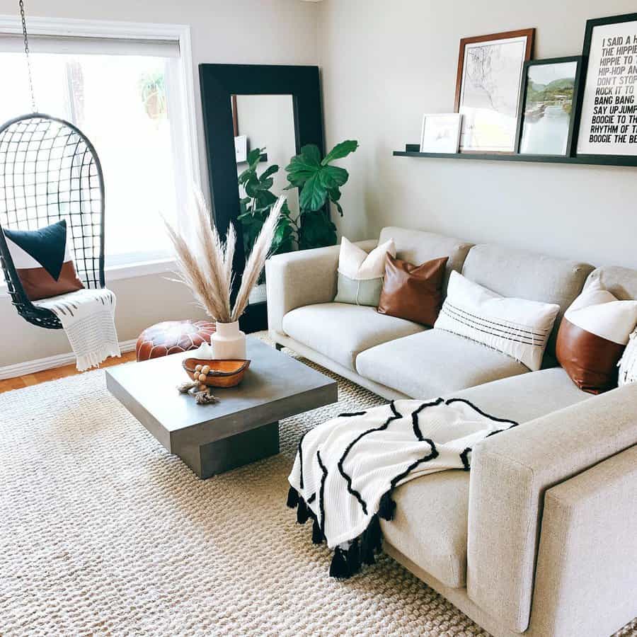 Modern boho living room with a neutral sectional, leather accent pillows, a black hanging chair, and a cozy textured rug for a warm, inviting feel