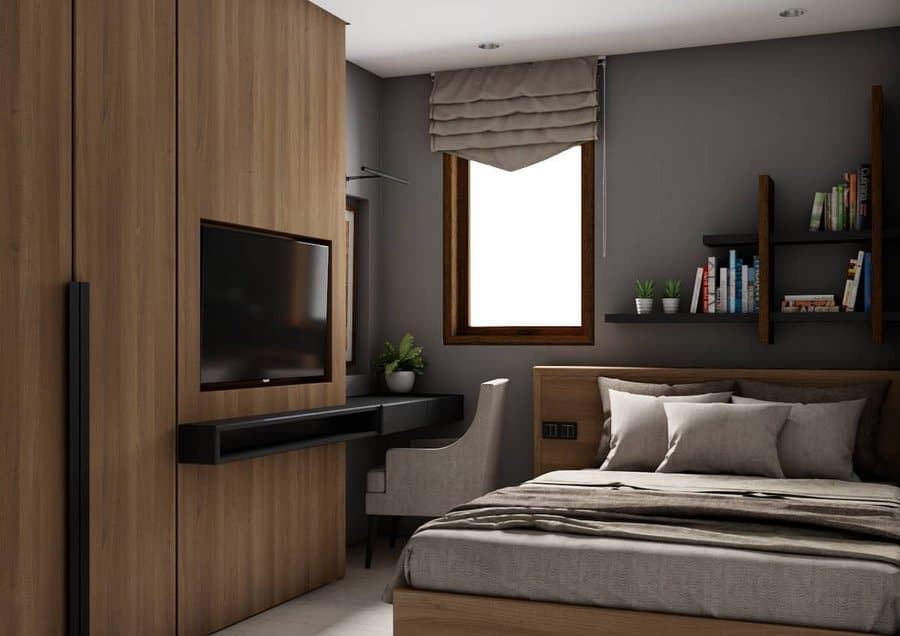 Modern bedroom with a wooden wardrobe, wall-mounted TV, window with a shade, desk with a chair, bookshelves, and a neatly made bed