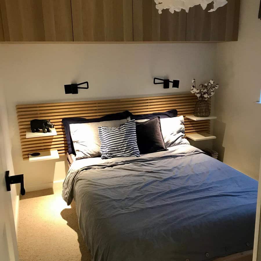 Cozy bedroom with a wooden headboard, wall-mounted lamps, blue-gray bedding, decorative pillows, and small nightstands flanking the bed