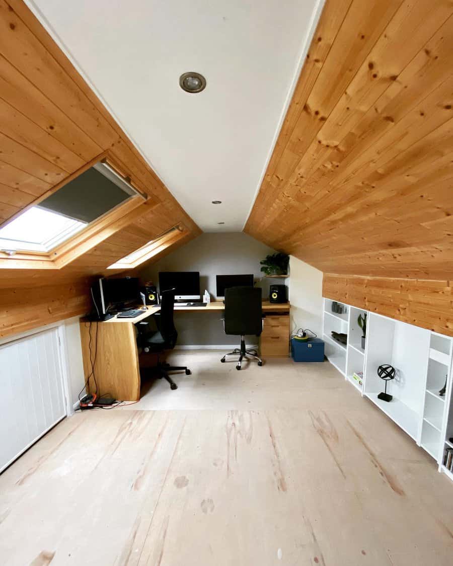 Modern attic workspace with wood-paneled ceilings, skylights, a built-in desk, and white shelving for storage and organization.