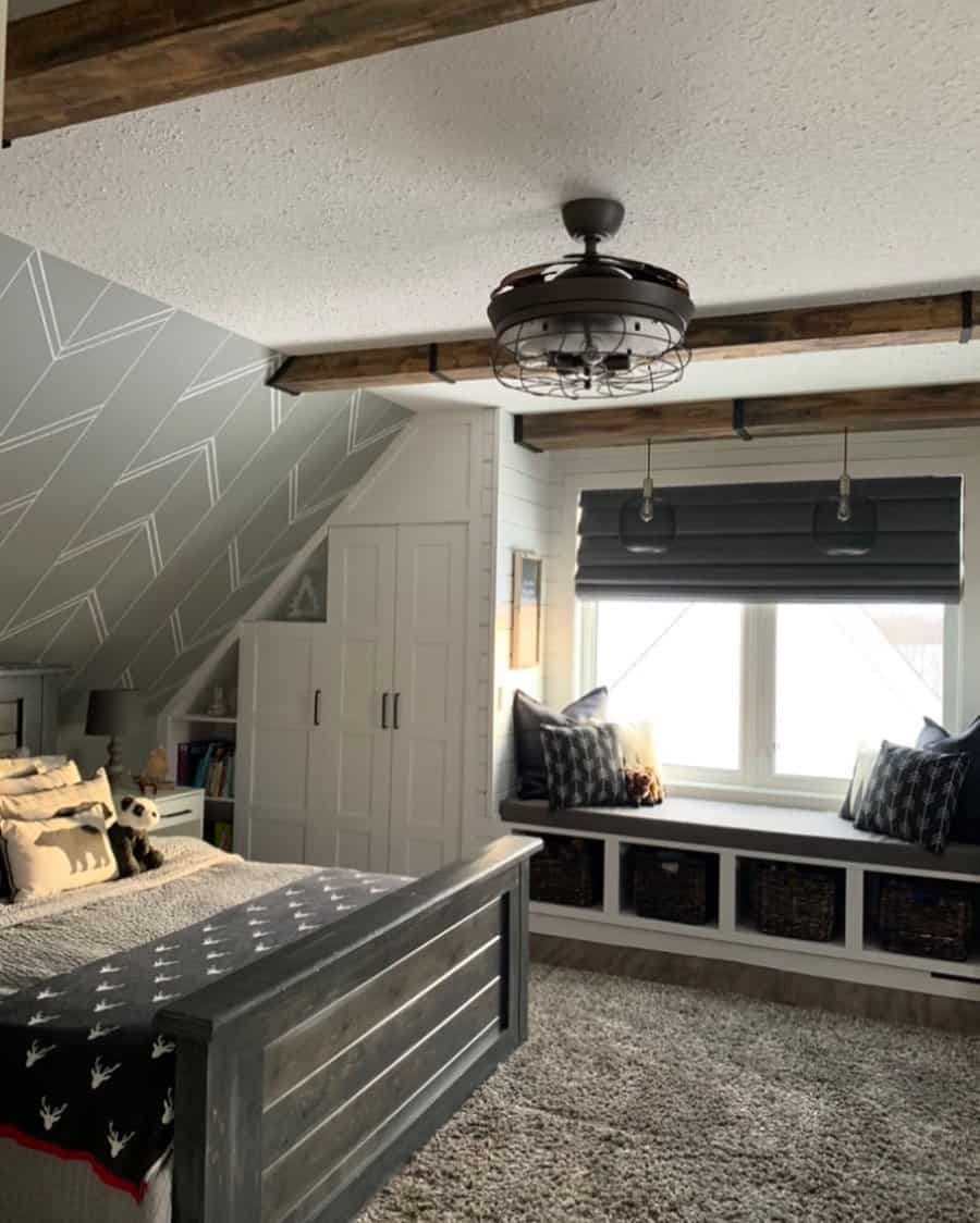 Cozy attic bedroom with a rustic wood bed, built-in storage, window seating with cushions, and exposed beams for a warm ambiance.