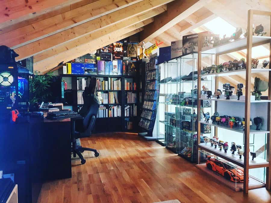 Attic gaming and collector's room with a wooden ceiling, bookshelves, glass display cases for collectibles, and a computer setup.