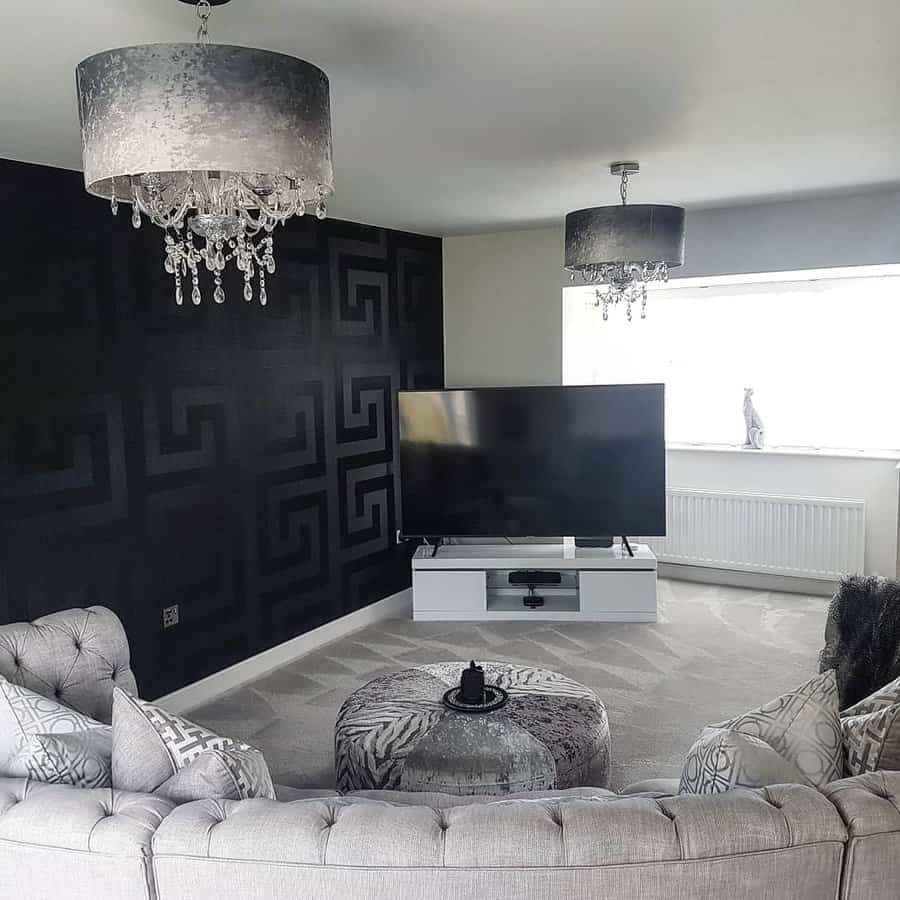 Modern living room with a gray tufted sofa, black accent wall, large TV on a white stand, and chandelier lighting