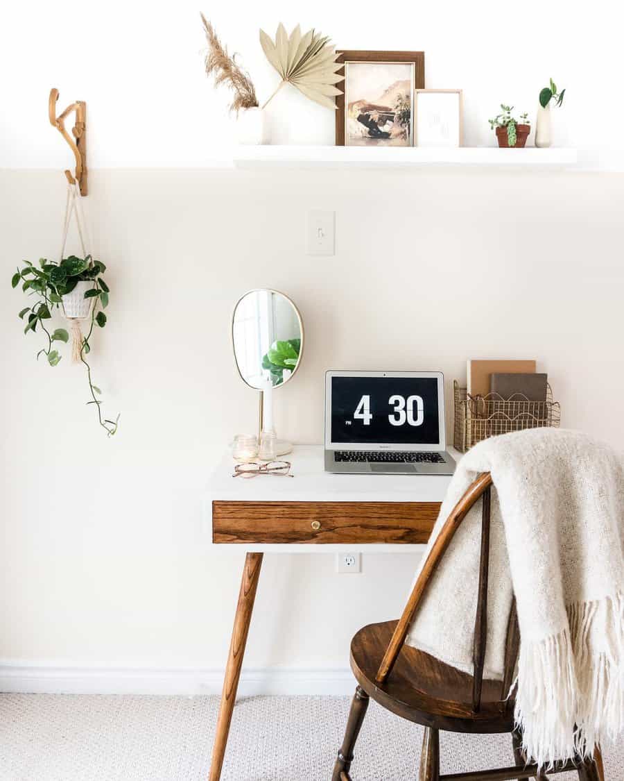 Minimalist workspace with a wooden desk, chair, laptop displaying 4:30, plants, mirror, and decorative items on a shelf above