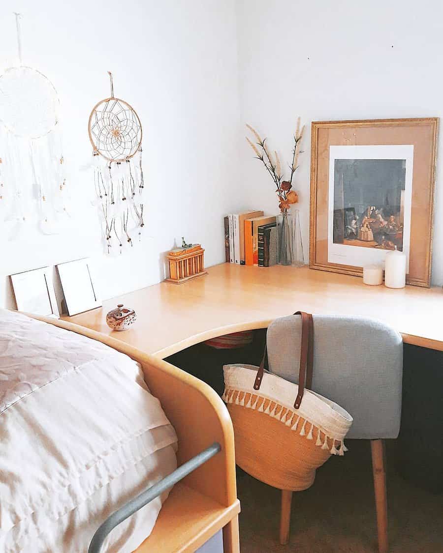 Cozy corner desk with books, framed art, and dreamcatchers on the wall; a chair with a bag is in front; minimalist decor