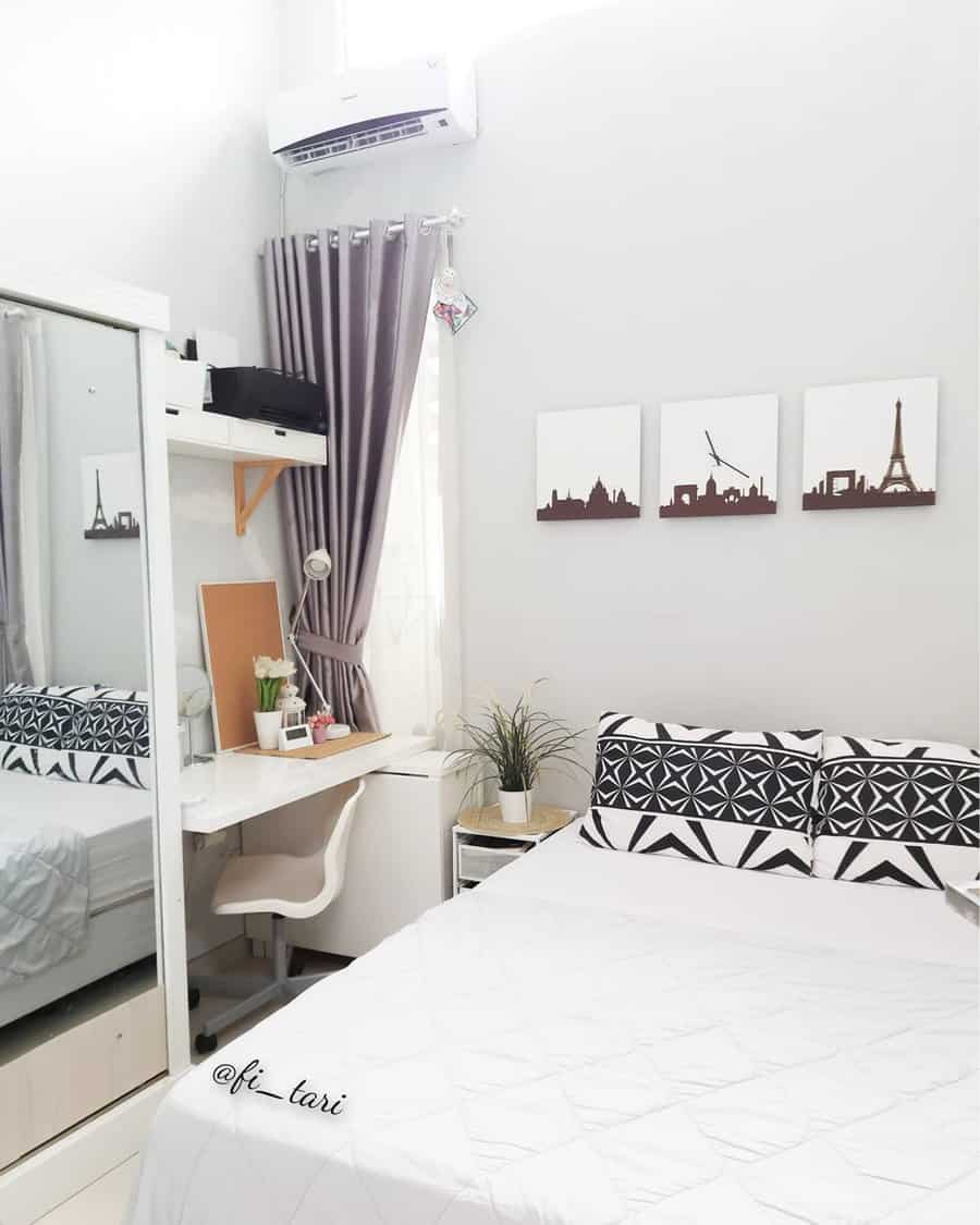 Minimalist bedroom with white decor, a bed, study desk, and mirror closet featuring wall art and potted plants as accents