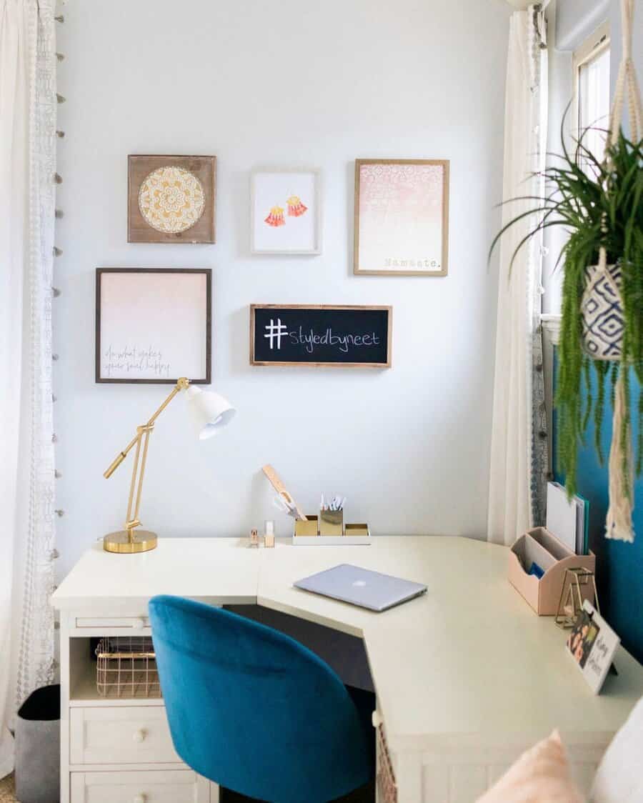 Chic corner bedroom office with a white L-shaped desk, gold accents, a teal velvet chair, and framed wall art for a stylish workspace