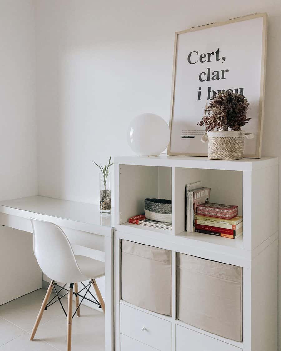 Minimalist home office with a white desk, chair, shelving unit, books, and decor; framed art and potted plants add a cozy touch