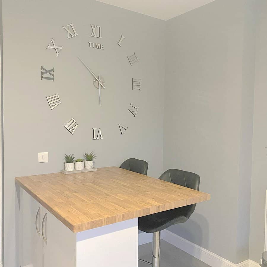 Minimalist corner breakfast bar with a wooden countertop, black barstools, and a large Roman numeral wall clock for a modern touch