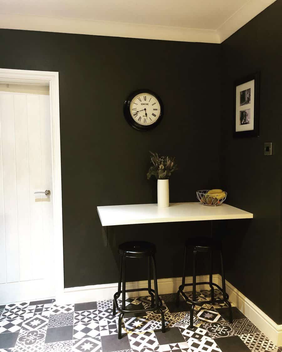 Stylish corner breakfast bar with a white floating tabletop, black stools, dark walls, and patterned tile flooring for a bold, modern look