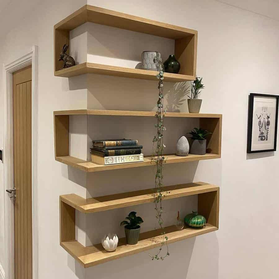 Wooden zigzag wall shelves with plants, books, and decor items; a hanging plant trails down the middle; white walls and a wooden door