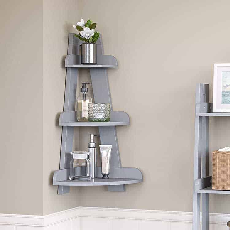 Gray corner shelf with three tiers, holding a potted plant, candle, dispenser, cup, and tube against a beige wall