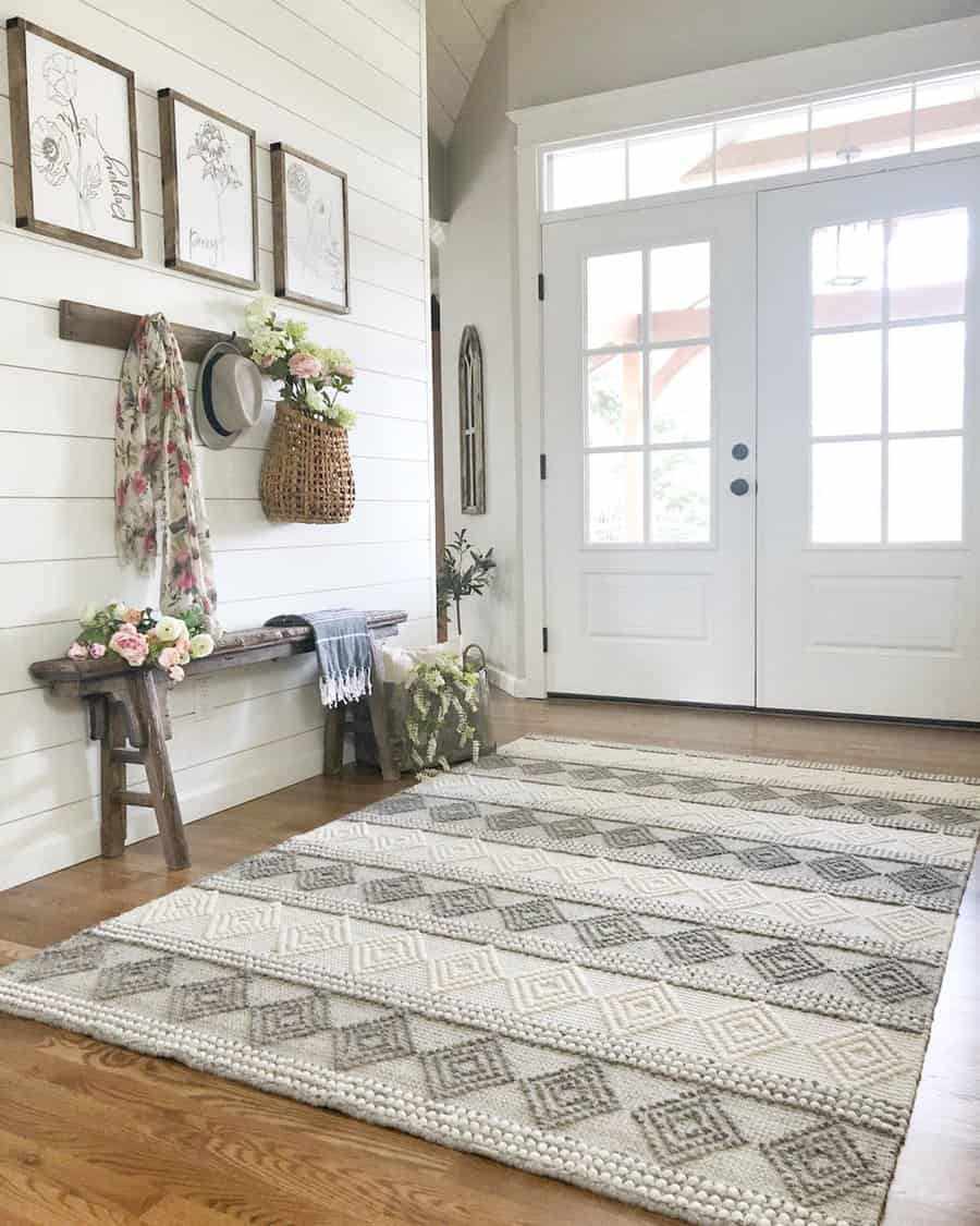 Bright farmhouse entryway with a rustic wooden bench, shiplap walls, floral accents, and a woven basket, creating a warm and inviting space