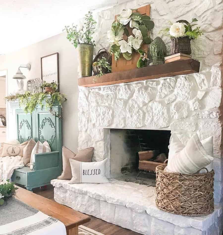 Cozy living room with a stone fireplace, decorative plants, a woven basket, and pillows on the mantel and floor