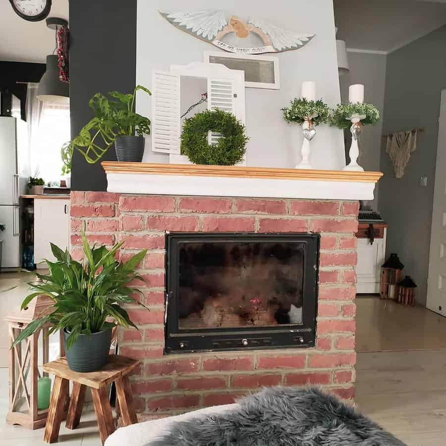 A cozy living room with a red brick fireplace, green plants, decorative wreaths, and candles on the mantle