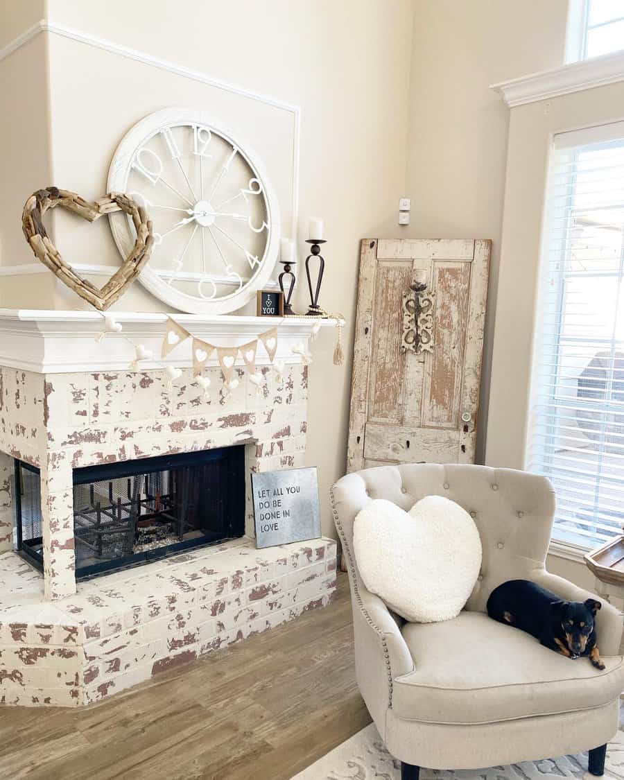 Cozy living room with a rustic fireplace, large clock, heart decor, and a chair with a heart pillow; a small dog rests on the chair