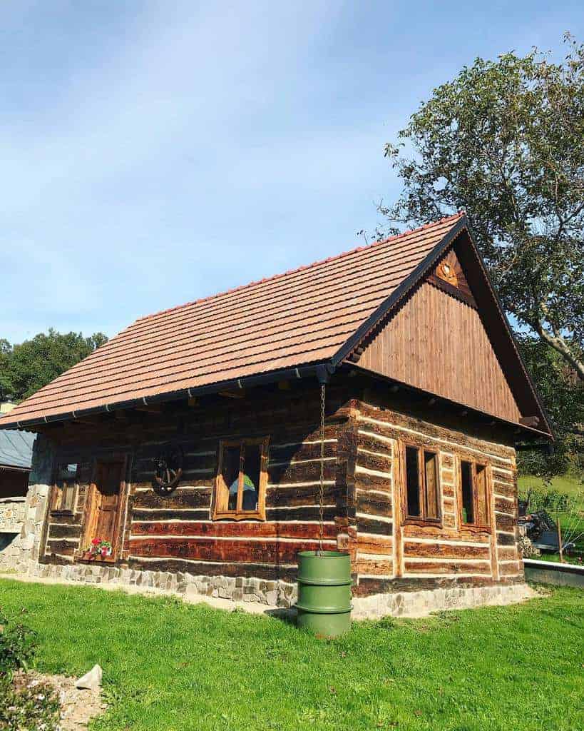 A small wooden cabin with a red-tiled roof set in a grassy area under a blue sky