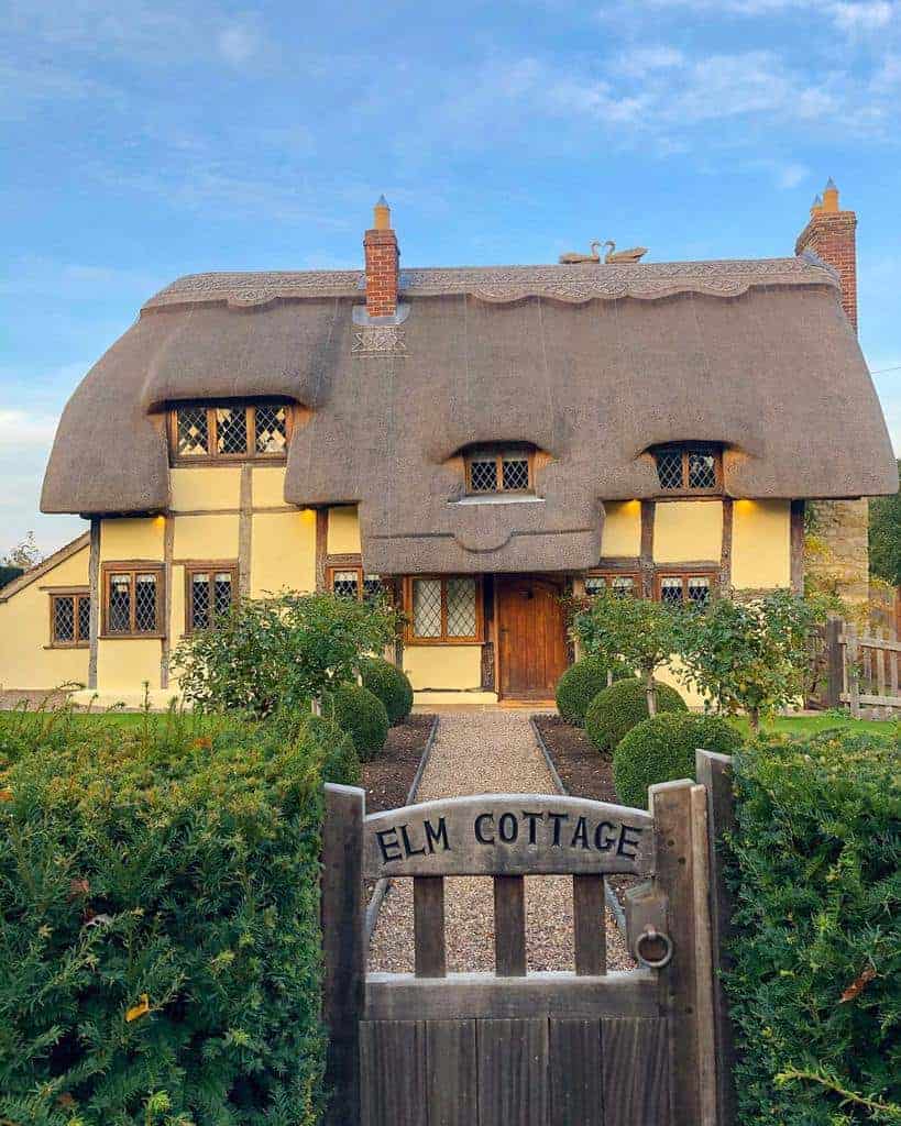 A charming cottage with a thatched roof and manicured garden, sign reads "Elm Cottage"