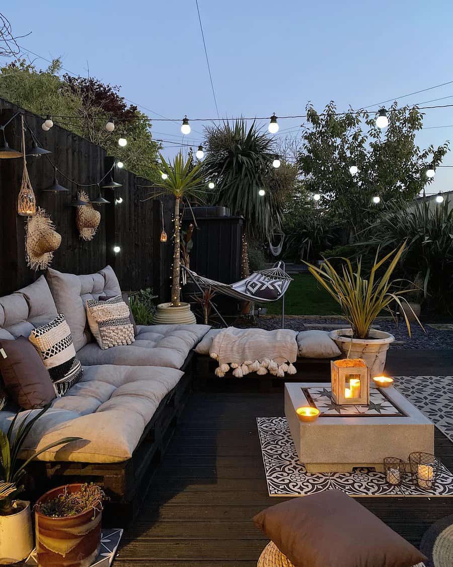 Cozy outdoor patio at dusk with string lights, cushioned seating, a table with candles, potted plants, and a hammock in the background