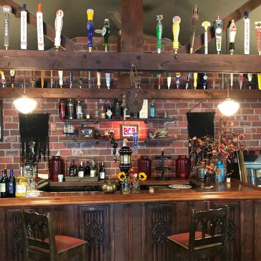 A rustic home bar with wooden decor, shelves of beer taps, bottles, sunflowers on the counter, and a brick wall backdrop