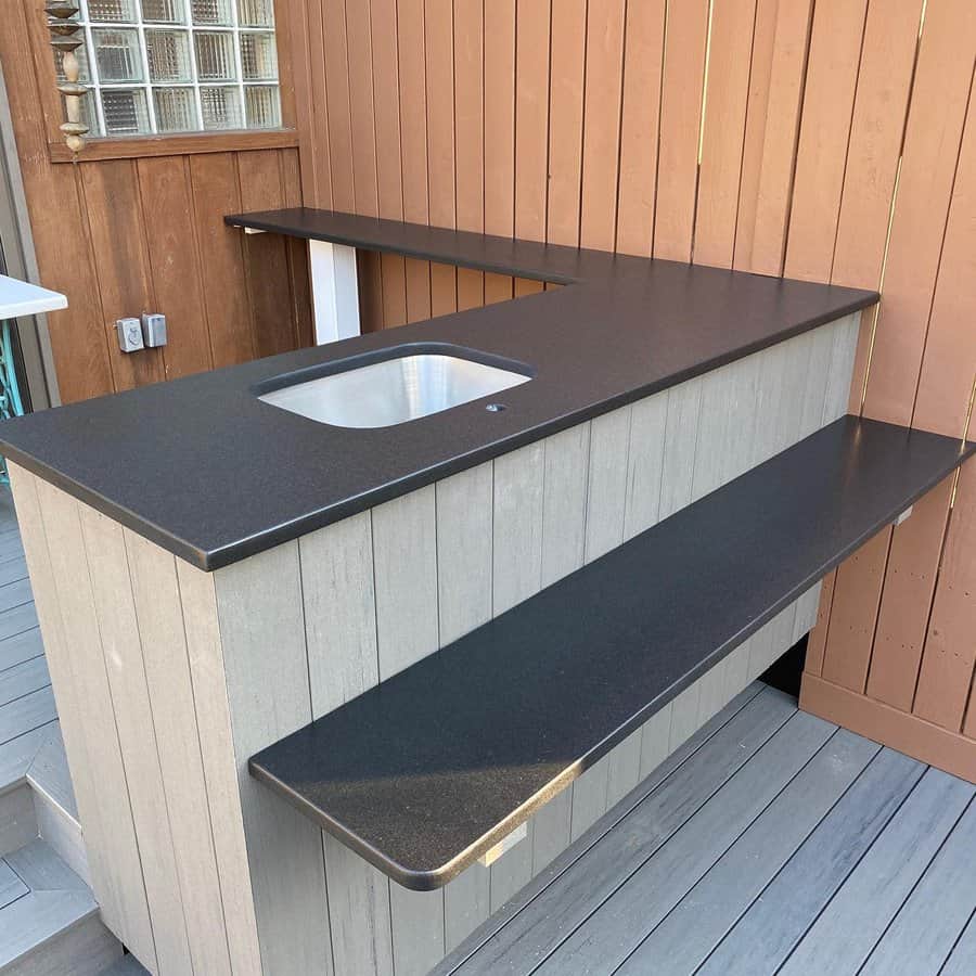 L-shaped wooden outdoor bar with black countertops and a built-in sink