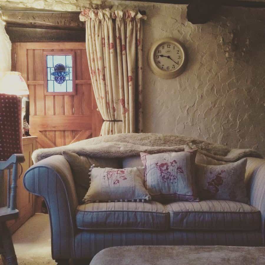 Cozy cottage living room with a vintage striped sofa, floral pillows, warm lighting, rustic wooden door, and textured stone walls for a timeless charm