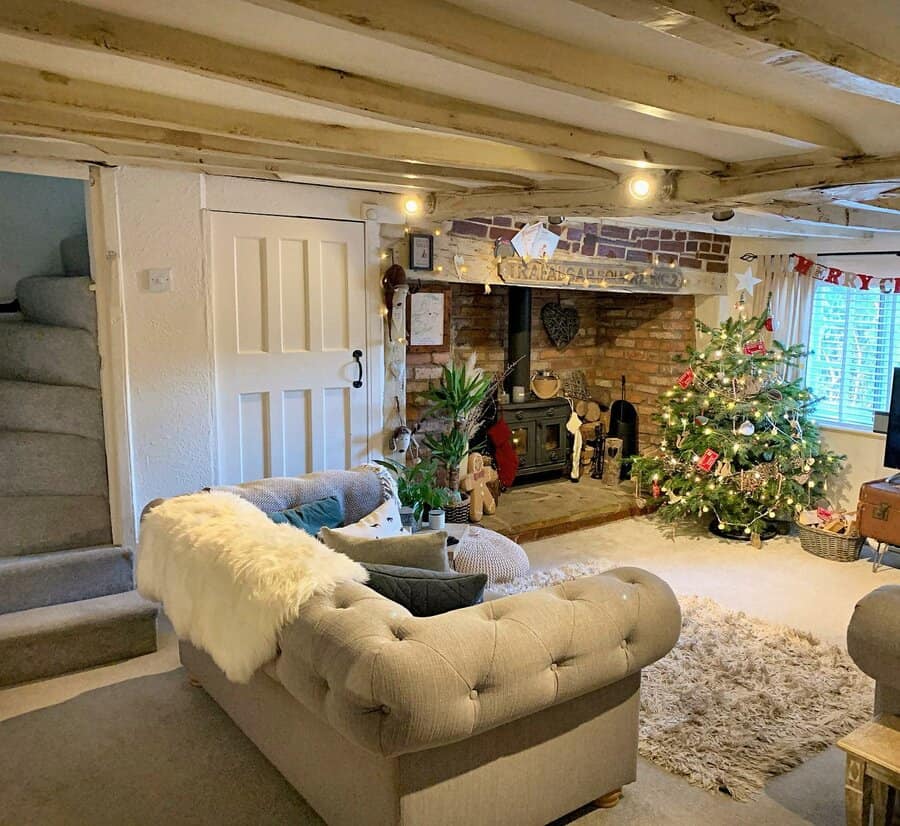 Rustic cottage living room with exposed beams, a tufted sofa, a brick fireplace, and a festive Christmas tree creating a warm, inviting atmosphere