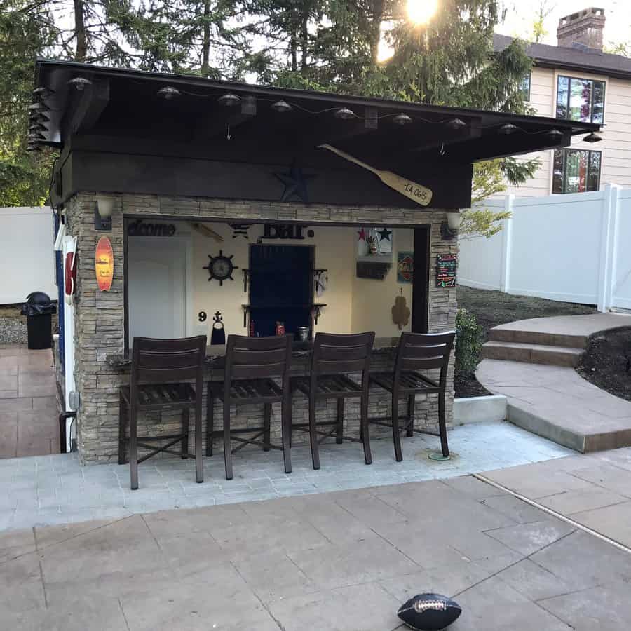 Stone-clad backyard bar with nautical decor, a dark roof, and barstools, creating a stylish outdoor entertainment space