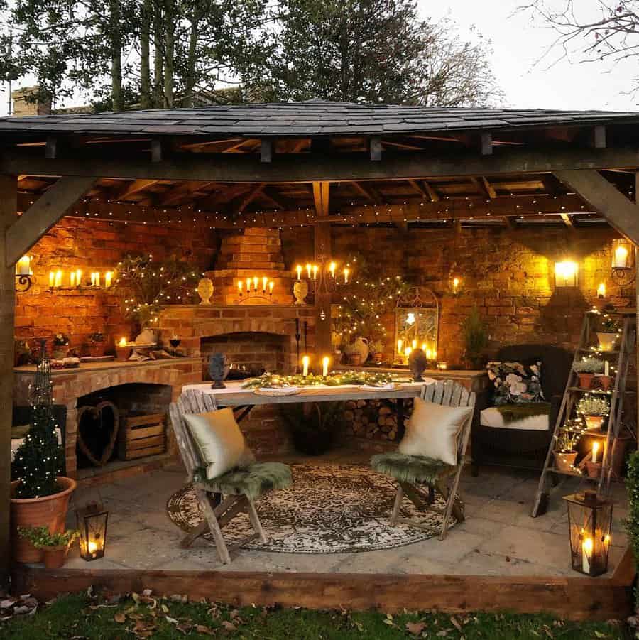 Cozy outdoor patio with a wooden roof, fairy lights, a table set for two, candles, potted plants, and a brick fireplace