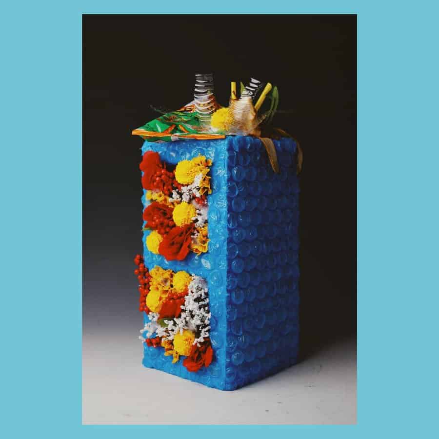 Creative cinder block craft covered in blue bubble wrap, decorated with vibrant flowers and artistic elements, resembling a unique miniature building