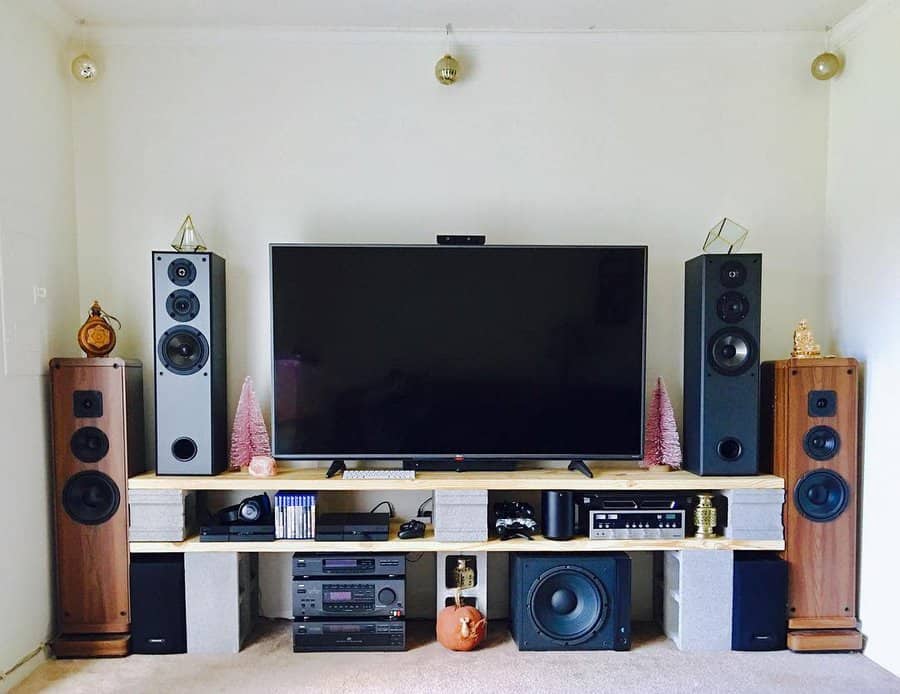 DIY entertainment center made from cinder blocks and wooden planks, supporting a large TV, speakers, and decor for a modern and functional setup