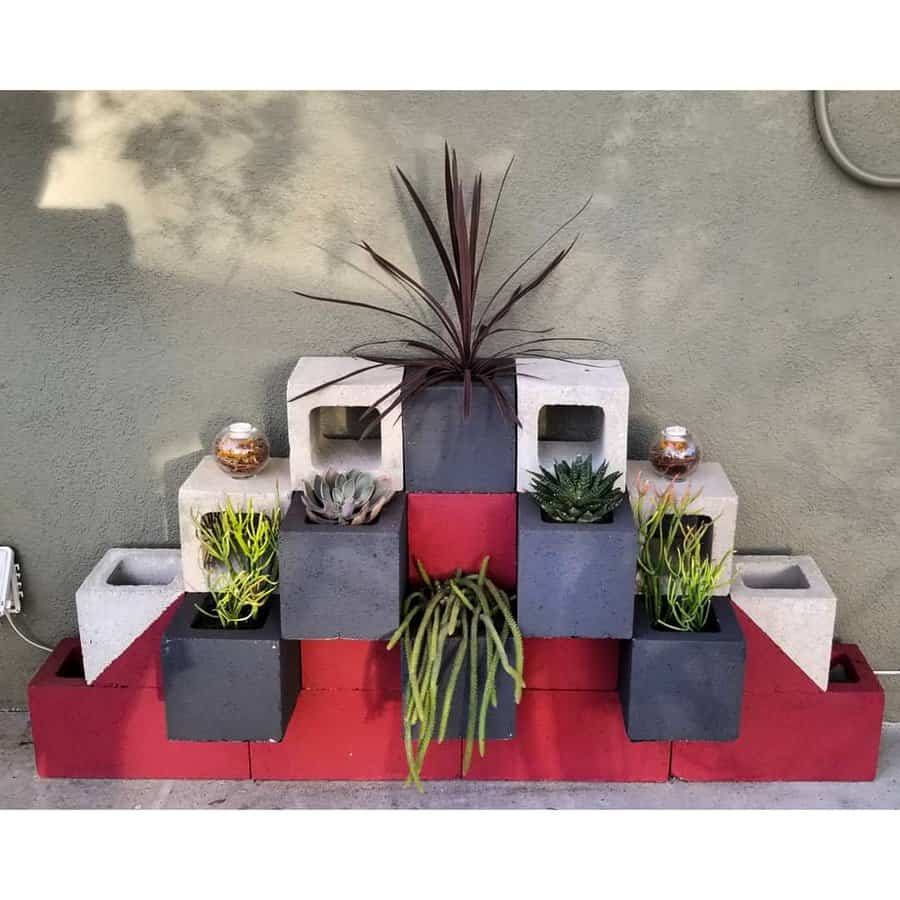 Modern cinder block planter display with red, black, and white blocks arranged in a tiered design, showcasing succulents and greenery against a wall