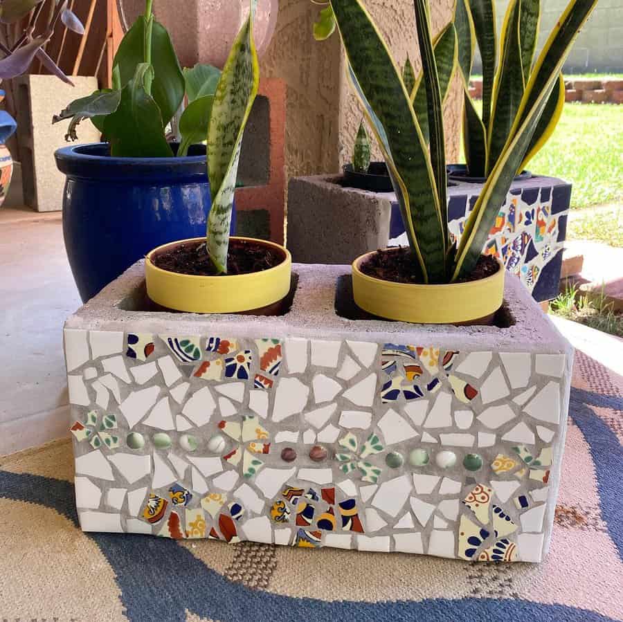 Decorative cinder block planter with mosaic tile design, holding two potted snake plants, adding a colorful and artistic touch to an outdoor space