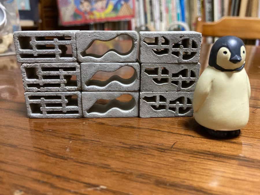 Miniature cinder blocks with intricate cutout designs stacked on a wooden surface, next to a small penguin figurine, creating a unique display