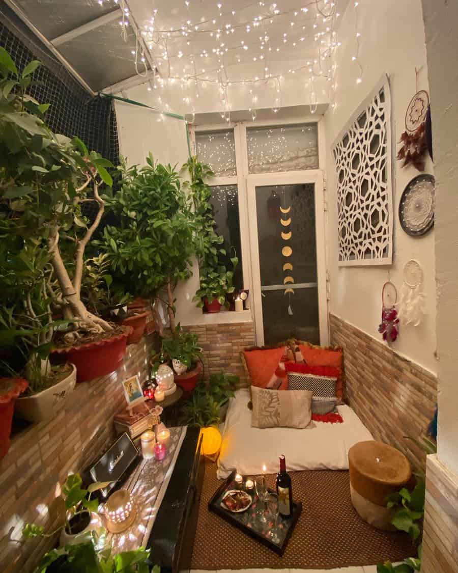 Cozy small balcony with fairy lights, floor seating, warm-toned pillows, lush plants, candles, and a romantic dinner setup