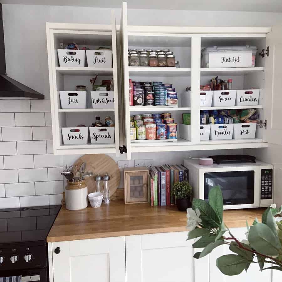 Organized kitchen cabinets with labeled storage bins for snacks, spices, canned goods, and essentials, creating a neat and tidy space