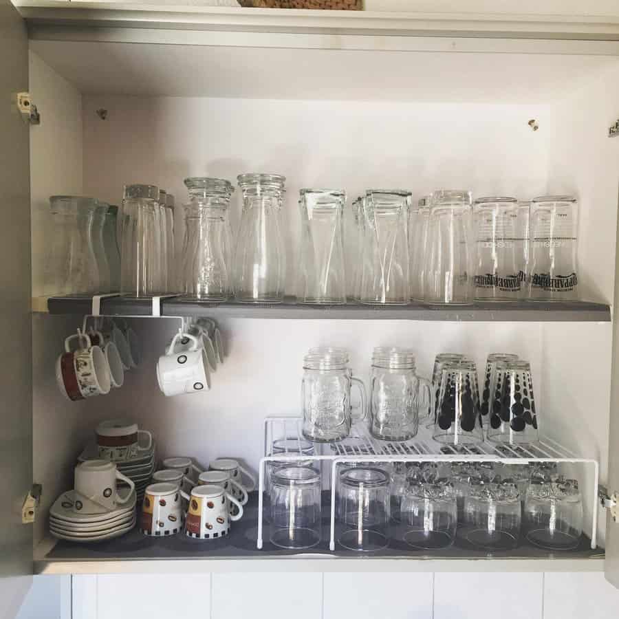 Neatly organized kitchen cabinet with glassware, mugs, and cups stored using racks and hooks for efficient space-saving storage