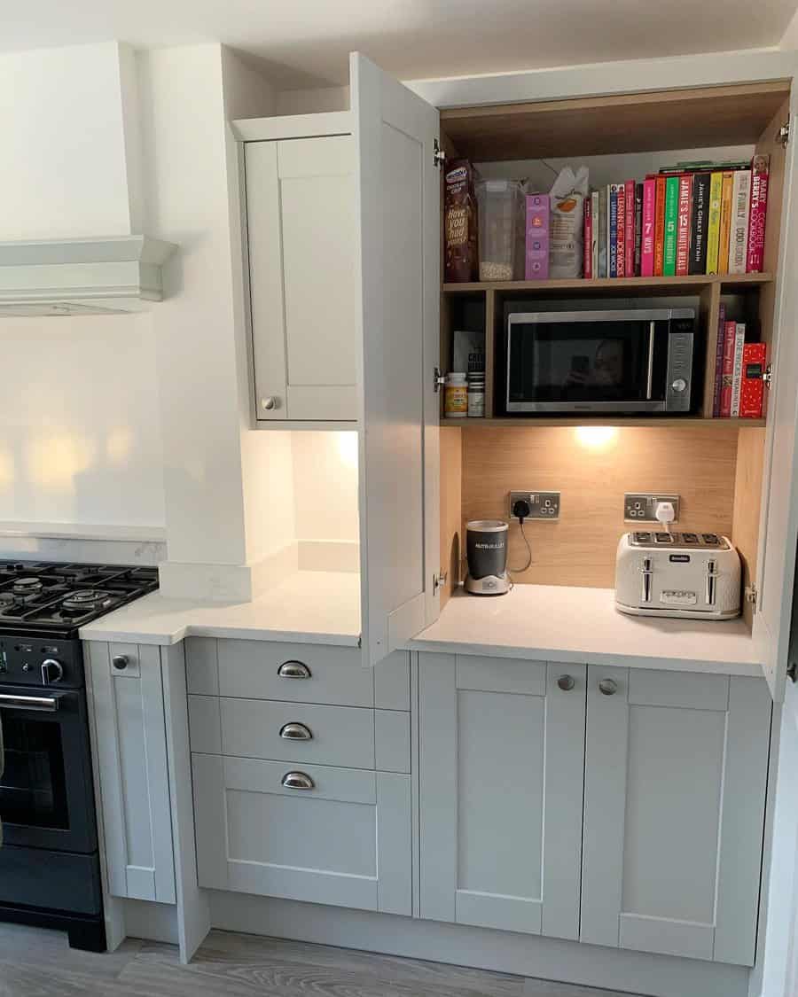 Compact kitchen cupboard with built-in microwave, cookbooks, pantry essentials, and small appliances neatly stored for convenience