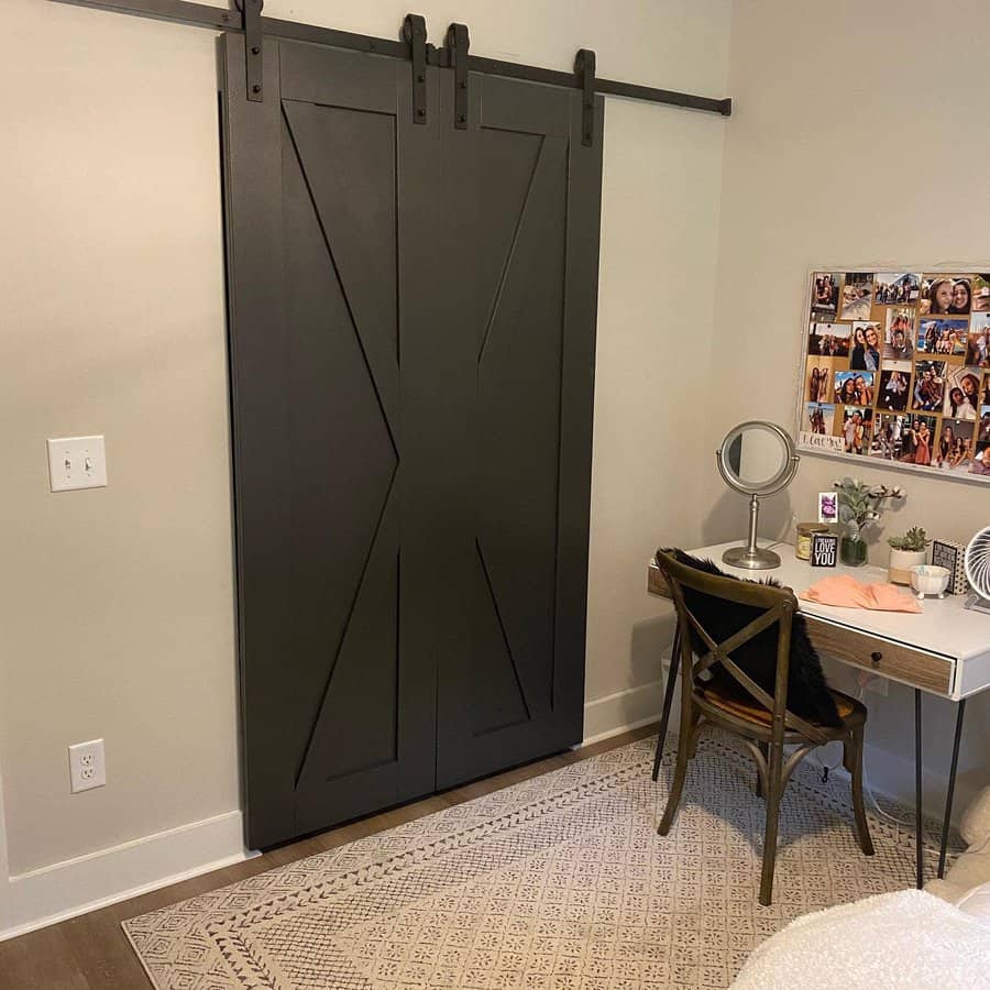 Bedroom with dark sliding barn door, desk with mirror, chair, and a collage of photos on the wall; rug on wooden floor