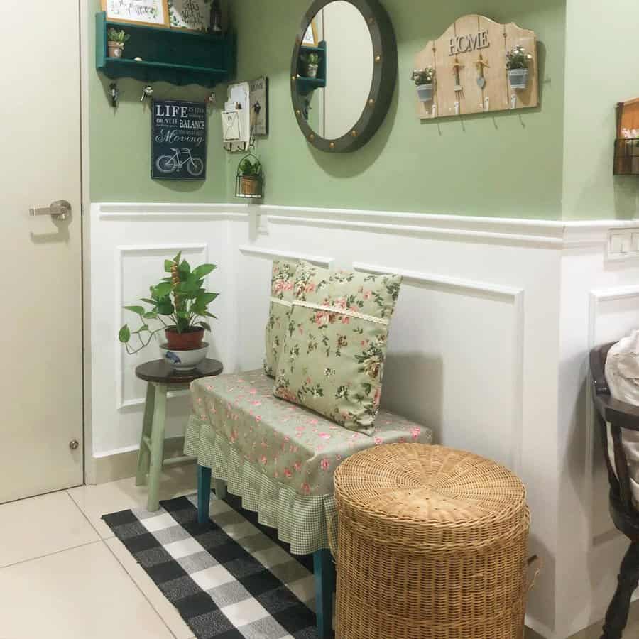 A cozy entryway with a floral cushioned bench, round mirror, wicker basket, small table with a plant, and decorative shelves on green walls