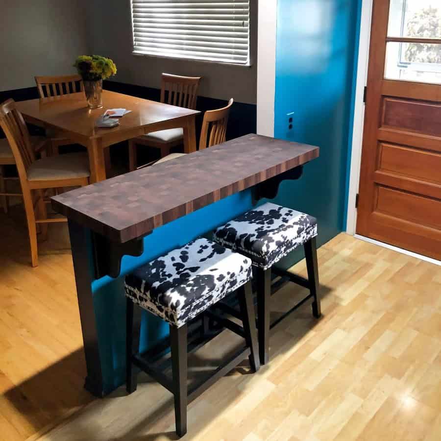 Small bar area with two black and white stools, wooden table with chairs in dining area, and a vase of flowers on the table