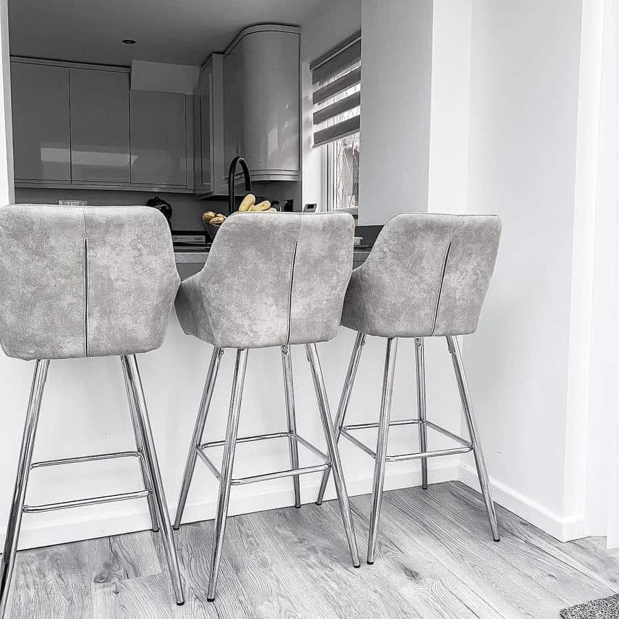 Three gray bar stools with metal legs at a modern kitchen counter, featuring sleek cabinetry and a bowl of bananas