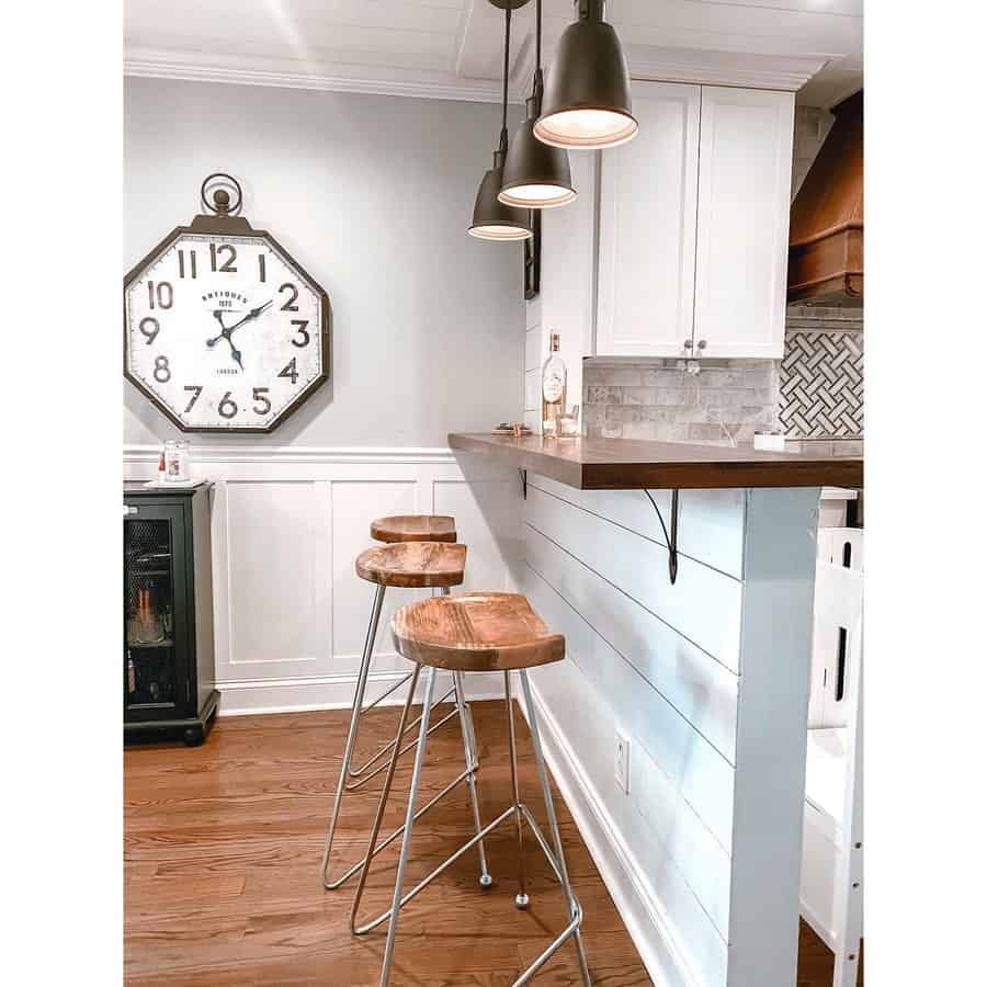 Rustic farmhouse-style breakfast bar with a wood countertop, white shiplap half-wall, industrial barstools, and black pendant lighting