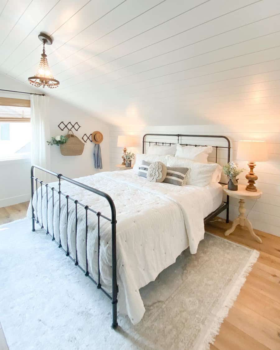 Bright farmhouse-style attic bedroom with a black metal bed frame, white shiplap walls, and warm wood accents. Soft textiles add cozy charm.