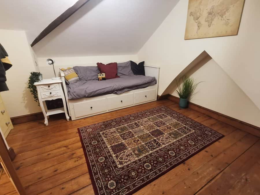 Cozy attic bedroom with a built-in daybed, warm wood flooring, and vintage decor. A rich patterned rug and soft lighting create a relaxed vibe.