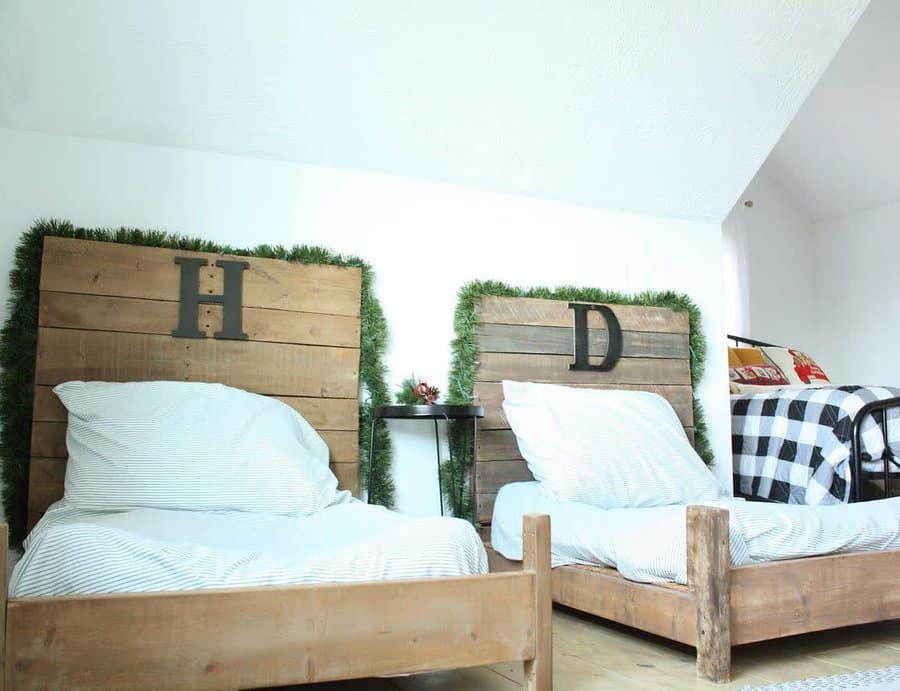 Rustic attic bedroom with wooden twin beds, personalized headboards, and festive greenery. Cozy farmhouse-inspired decor with a warm touch.