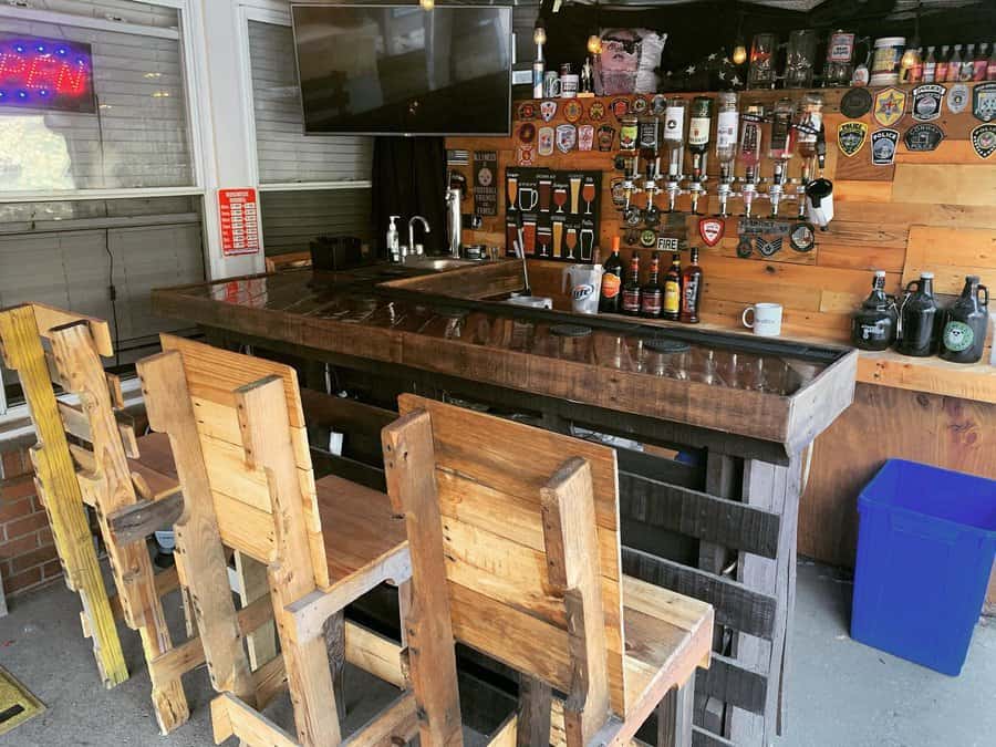 Wooden bar setup with rustic stools, a variety of draft beer taps, an overhead TV, and a wall decorated with badges and beer logos