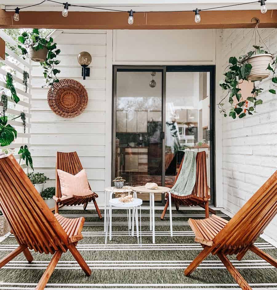 Cozy patio with wooden chairs, a small round table, plants, and string lights; decor includes a woven wall hanging and striped rug