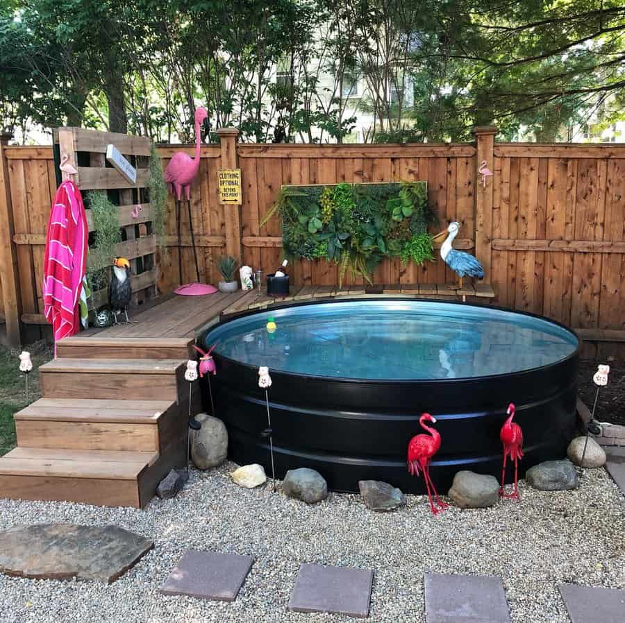 A small backyard pool setup with flamingo decorations, wooden deck, and potted plants next to a wooden fence